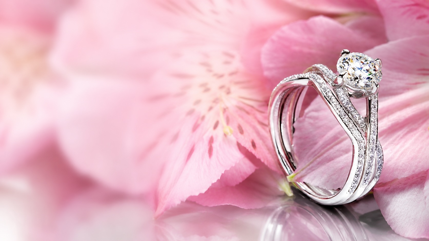 Simon G diamond engagement ring with a round brilliant centre stone on a soft pink floral background.